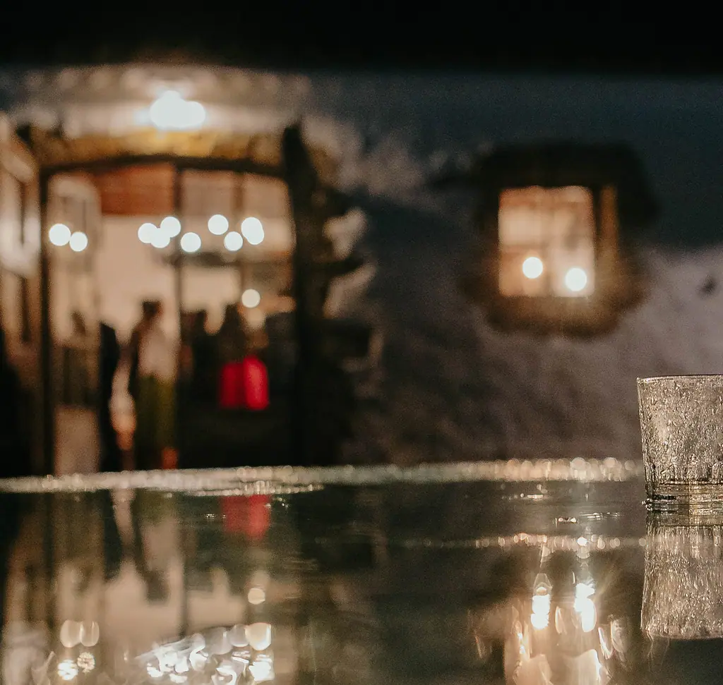 A crystal glass on a candlelit table at night, a villa glowing behind