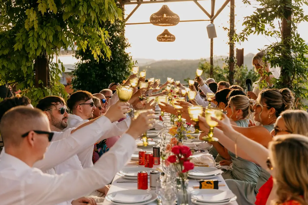Guests raising their glasses at a long table at golden hour, the hills behind