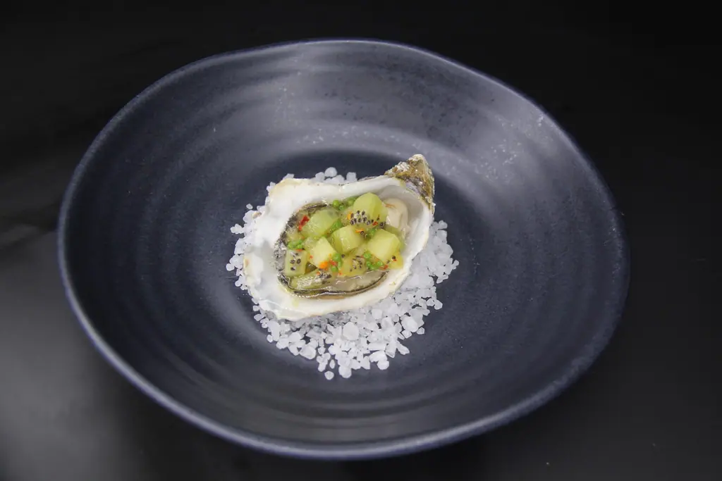 An oyster served on crushed ice in a dark stoneware bowl