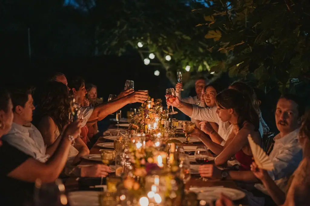 Guests raising a toast at a long candlelit table at night
